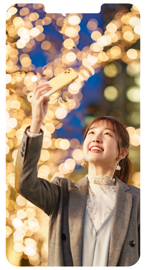 女性がスマートフォンをかざしてイルミネーションの写真を撮っている