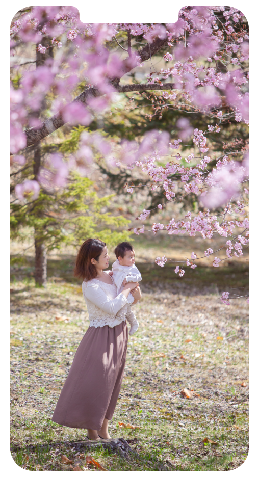 桜の木の下でお母さんが赤ちゃんを抱っこして花見をしている