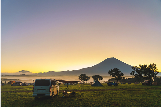 遠くに山が見え夕日の景色が広がっているキャンプ場でテントが張られている